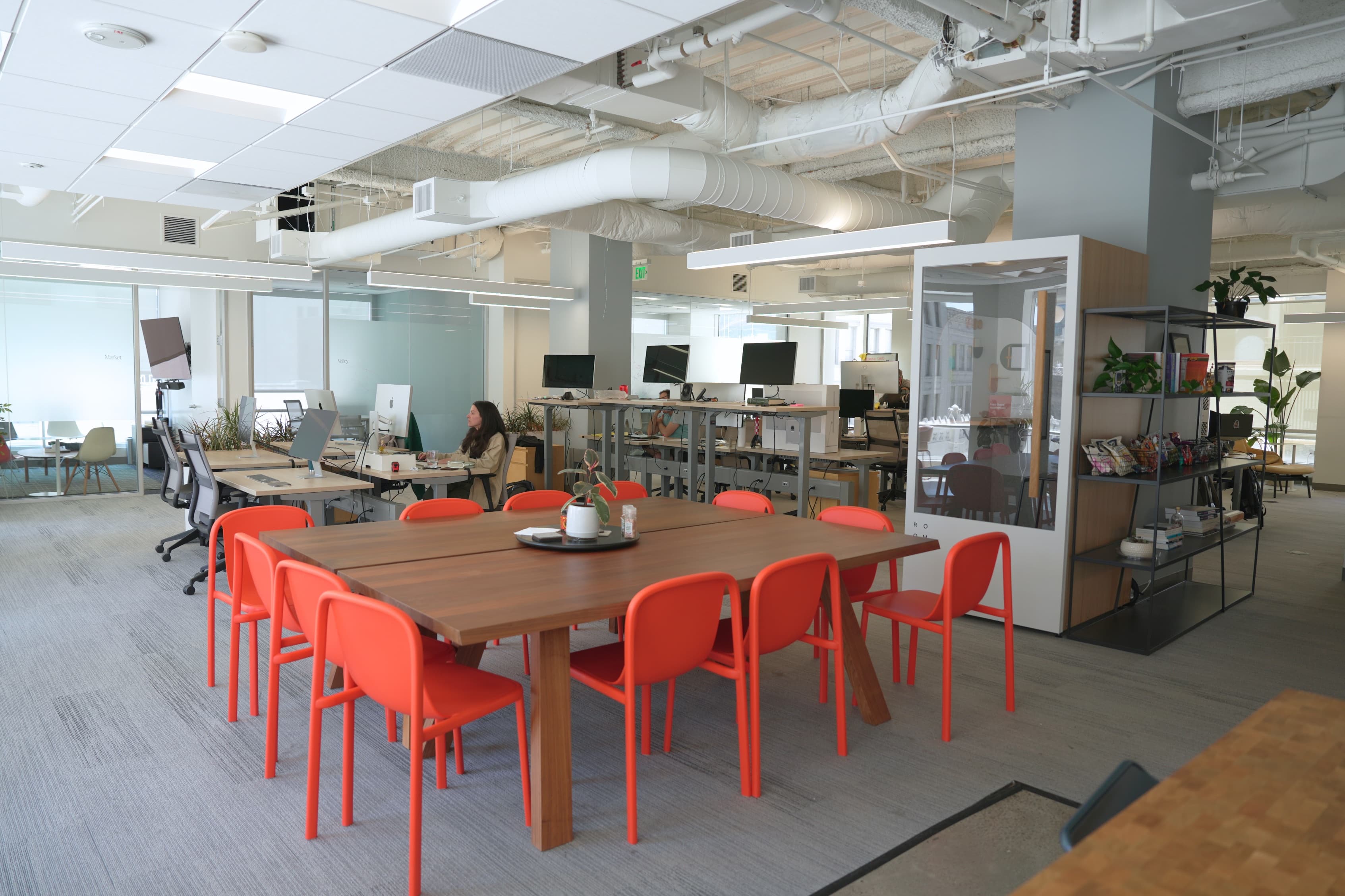 Town's San Francisco office — an open-plan workspace with a wood communal table, orange chairs, sit-stand desks, and the team at work.